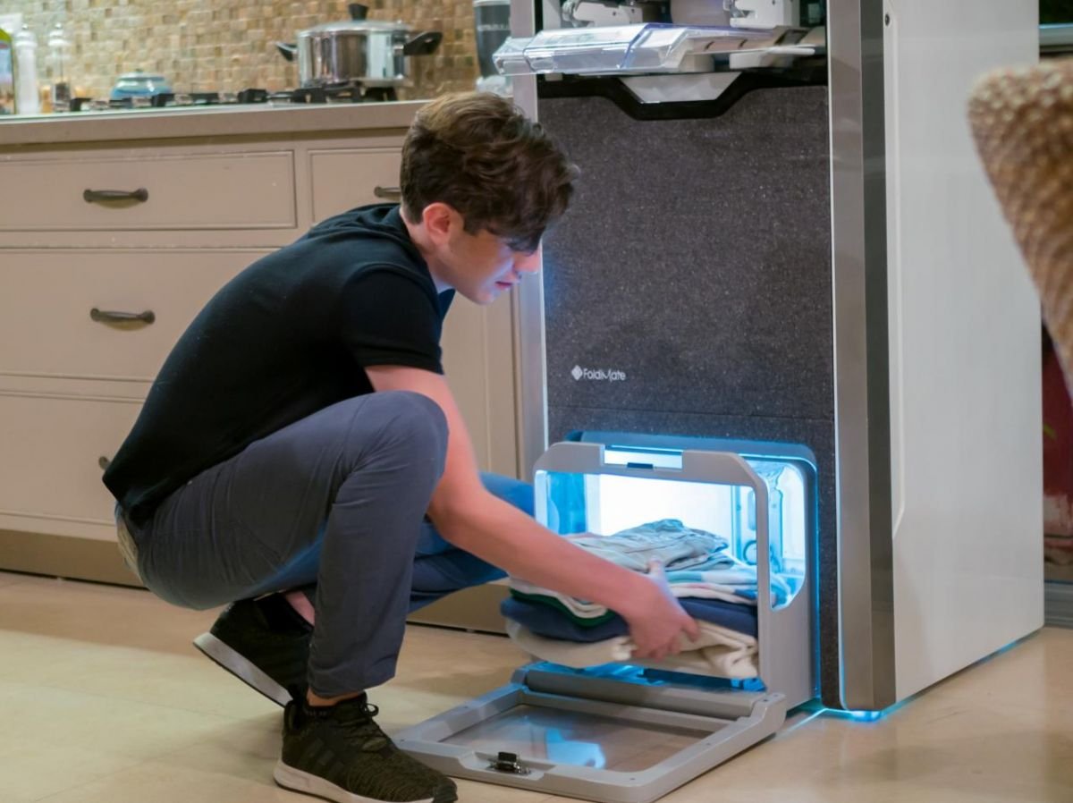 A young boy removes his impeccably folded and ironed clothes from the FoldiMate machine, offering fast, quality results. Find out how this innovative solution simplifies folding and ironing on foldimateofficial.com.